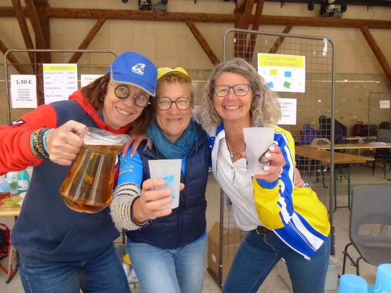 Trois bénévoles souriantes trinquent avec un pichet de boisson au ravitaillement de la Coublevitaine.