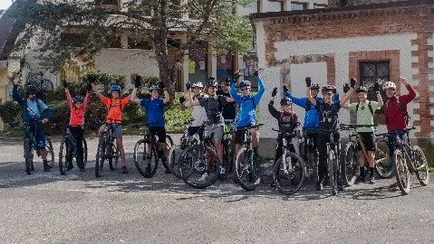 Une quinzaine de jeunes de la Team J sur leurs VTT, bras levés, devant un bâtiment en briques.