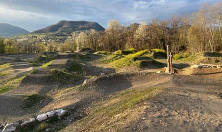 Les bosses de terre du bike park La Pioche au soleil couchant, montagnes en fond.