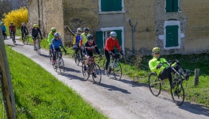 Groupe route en file sur une petite route de campagne, au printemps, devant une vieille ferme aux volets verts.