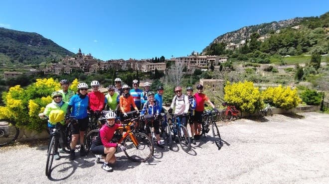 Groupe du club posant avec les vélos devant un village perché du Sud, genêts en fleurs.
