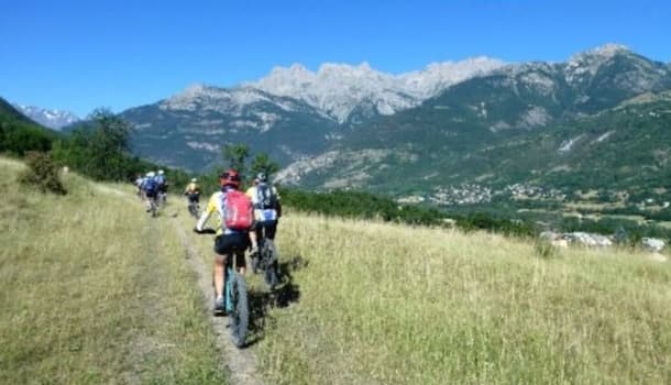 Vététistes du club en file sur un sentier herbeux, face à une crête calcaire.