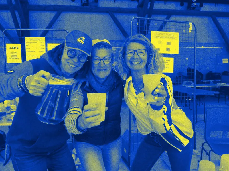 Trois bénévoles souriantes à la buvette de la Coublevitaine, l'une tient un pichet, les autres des gobelets.