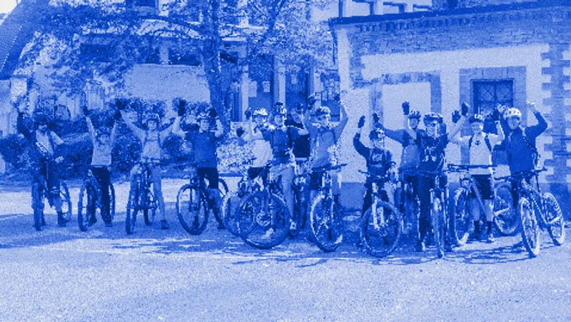 Une vingtaine de jeunes vététistes casqués lèvent les bras devant un bâtiment en pierre.